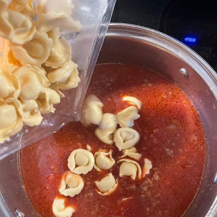 adding cheese tortellini to pot of soup